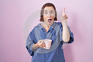 Middle age hispanic woman drinking a cup coffee pointing finger up with successful idea