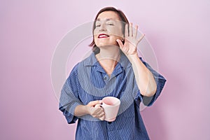 Middle age hispanic woman drinking a cup coffee smiling with hand over ear listening an hearing to rumor or gossip