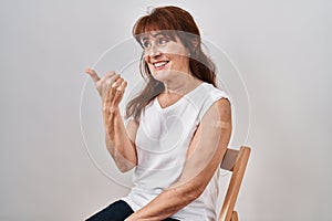 Middle age hispanic woman getting vaccine showing arm with band aid smiling with happy face looking and pointing to the side with