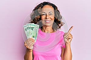 Middle age hispanic woman holding 10000 south korean won banknotes smiling happy pointing with hand and finger to the side