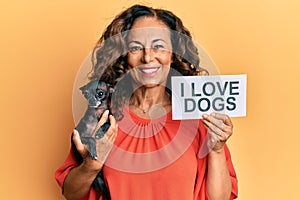 Middle age hispanic woman holding chihuahua dog and paper with i love dogs phrase smiling with a happy and cool smile on face