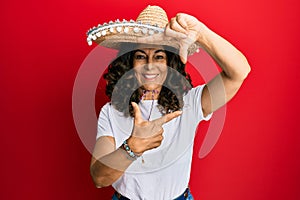 Middle age hispanic woman holding mexican hat smiling making frame with hands and fingers with happy face