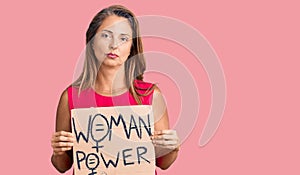 Middle age hispanic woman holding woman power banner thinking attitude and sober expression looking self confident