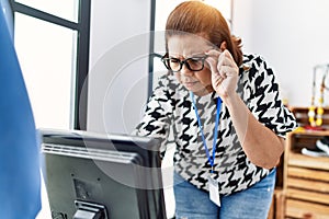 Middle age hispanic woman looking computer working at clothing store