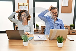 Middle age hispanic woman and man sitting with laptop at the office confuse and wonder about question