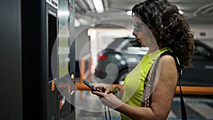 Middle age hispanic woman paying at parking machine parking