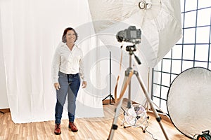 Middle age hispanic woman posing as model at photography studio looking positive and happy standing and smiling with a confident