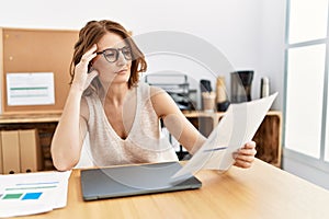 Middle age hispanic woman reading paperwork working at office