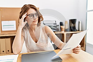 Middle age hispanic woman reading paperwork working at office