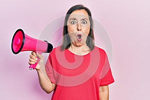 Middle age hispanic woman shouting through megaphone scared and amazed with open mouth for surprise, disbelief face