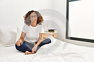 Middle age hispanic woman sitting on the bed at home winking looking at the camera with sexy expression, cheerful and happy face