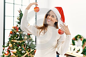 Middle age hispanic woman smiling confident holding christmas balls at home
