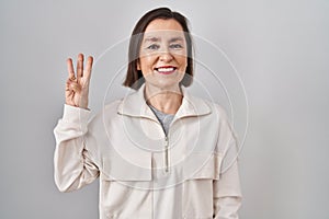 Middle age hispanic woman standing over isolated background showing and pointing up with fingers number three while smiling