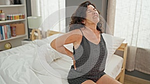 Middle age hispanic woman suffering for back injury sitting on bed at bedroom