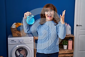 Middle age hispanic woman waiting for laundry celebrating victory with happy smile and winner expression with raised hands