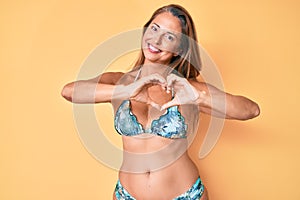 Middle age hispanic woman wearing bikini smiling in love showing heart symbol and shape with hands