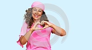 Middle age hispanic woman wearing breast cancer support pink scarf smiling in love showing heart symbol and shape with hands