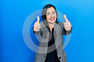Middle age hispanic woman wearing business clothes approving doing positive gesture with hand, thumbs up smiling and happy for