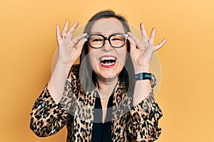 Middle age hispanic woman wearing business clothes and holding glasses smiling and laughing hard out loud because funny crazy joke