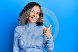 Middle age hispanic woman wearing casual clothes smiling with happy face looking and pointing to the side with thumb up