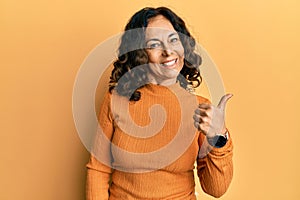 Middle age hispanic woman wearing casual clothes smiling with happy face looking and pointing to the side with thumb up