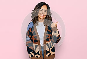 Middle age hispanic woman wearing casual clothes smiling with happy face looking and pointing to the side with thumb up