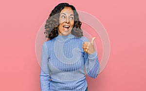 Middle age hispanic woman wearing casual clothes smiling with happy face looking and pointing to the side with thumb up