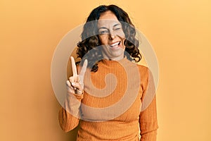 Middle age hispanic woman wearing casual clothes smiling with happy face winking at the camera doing victory sign