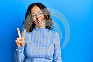 Middle age hispanic woman wearing casual clothes smiling with happy face winking at the camera doing victory sign