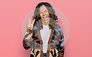 Middle age hispanic woman wearing casual clothes smiling with happy face winking at the camera doing victory sign