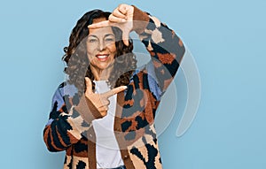 Middle age hispanic woman wearing casual clothes smiling making frame with hands and fingers with happy face