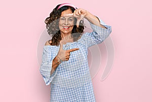 Middle age hispanic woman wearing casual clothes smiling making frame with hands and fingers with happy face