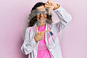 Middle age hispanic woman wearing doctor uniform and glasses smiling making frame with hands and fingers with happy face