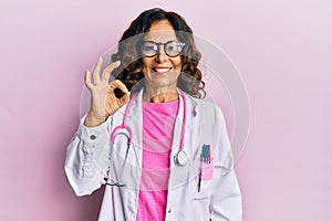 Middle age hispanic woman wearing doctor uniform and glasses smiling positive doing ok sign with hand and fingers