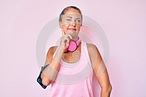 Middle age hispanic woman wearing gym clothes and using headphones serious face thinking about question with hand on chin,