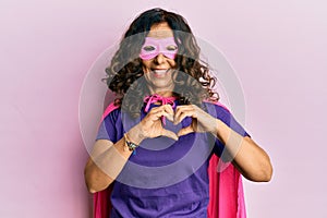 Middle age hispanic woman wearing super hero costume smiling in love doing heart symbol shape with hands