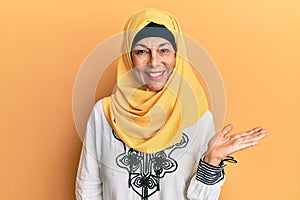 Middle age hispanic woman wearing traditional islamic hijab scarf smiling cheerful presenting and pointing with palm of hand