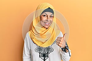 Middle age hispanic woman wearing traditional islamic hijab scarf smiling with happy face looking and pointing to the side with