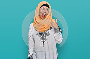 Middle age hispanic woman wearing traditional islamic hijab scarf smiling with happy face looking and pointing to the side with