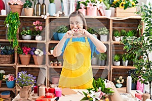 Middle age hispanic woman working at florist shop smiling in love doing heart symbol shape with hands