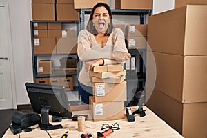 Middle age hispanic woman working at small business ecommerce angry and mad screaming frustrated and furious, shouting with anger