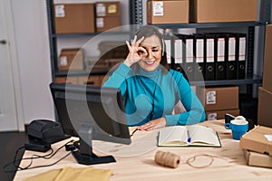 Middle age hispanic woman working at small business ecommerce on customer support smiling happy doing ok sign with hand on eye