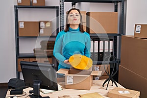 Middle age hispanic woman working at small business ecommerce preparing order looking at the camera blowing a kiss being lovely