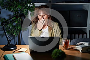 Middle age hispanic woman working using computer laptop at night bored yawning tired covering mouth with hand