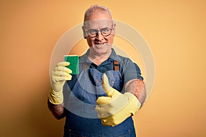 Middle age hoary cleaner man cleaning wearing apron and gloves using scourer happy with big smile doing ok sign, thumb up with