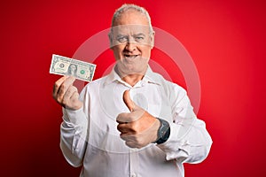 Middle age hoary man holding one dollar banknote over isolated red background happy with big smile doing ok sign, thumb up with