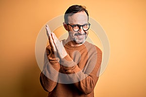 Middle age hoary man wearing brown sweater and glasses over isolated yellow background clapping and applauding happy and joyful,