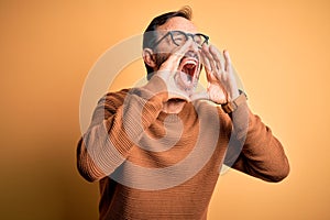 Middle age hoary man wearing brown sweater and glasses over isolated yellow background Shouting angry out loud with hands over