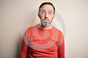 Middle age hoary man wearing casual orange sweater standing over isolated white background puffing cheeks with funny face