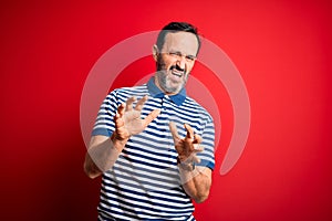 Middle age hoary man wearing casual striped polo standing over isolated red background disgusted expression, displeased and